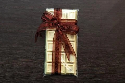 Tile of white chocolate in packaging with brown bow. Stock Photos