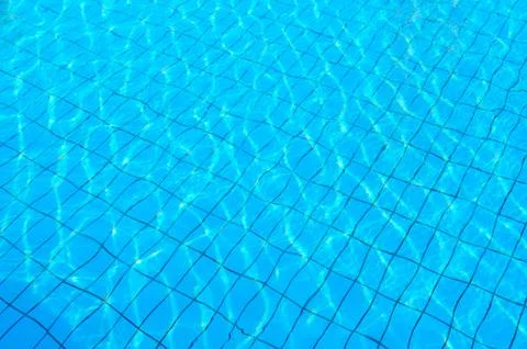 Tiled bottom of pool under transparent blue water with patches of sunlight Foto stock