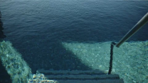 Tiled pool steps lead under a stainless handrail as a triangular shadow sweeps Stockbeeldmateriaal 329412776