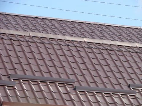 A tiled roof of a building with a wire loop on it and a blue sky at backgroun Stock Photos