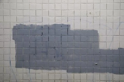 Tiled wall with a blank white bricks and gray spray painted graffiti. Stock Photos