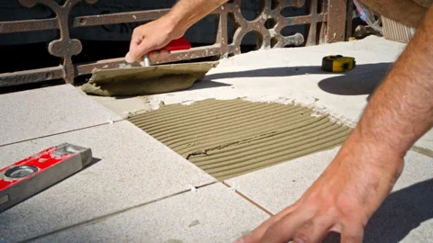 Tiler applying adhesive glue with notched trowel on outdoor terrace Video stock 263598207