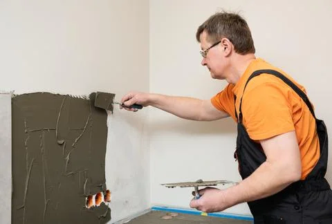 The tiler is applying adhesive to the kitchen wall to install the ceramic til Stock Photos