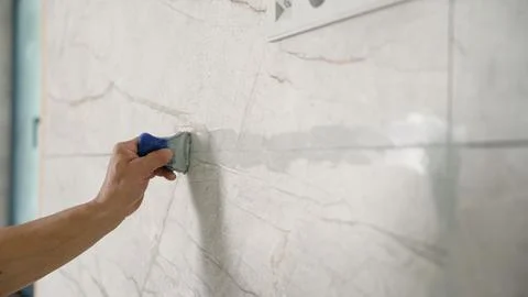 Tiler applying grout between large marble effect tiles on wall close up Stock Photos