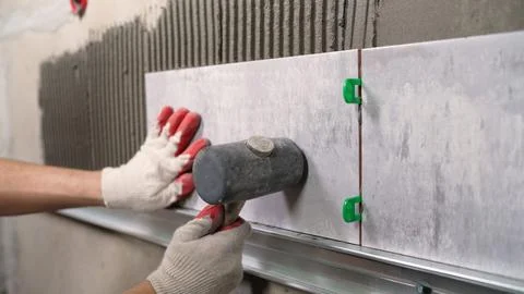 Tiler carefully using rubber mallet to adjust position of large format tile d Stock Photos