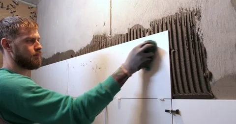 Tiler cleans with rag ceramic tile just laid on wall, rinses stains from mortar Stock Footage 130777652