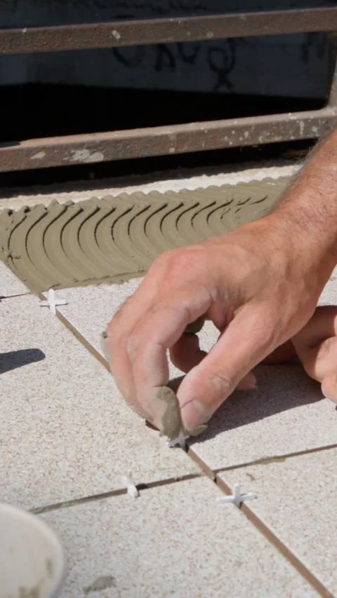 Tiler hand placing plastic cross spacers between ceramic tiles for leveling. Stock Footage 328411650
