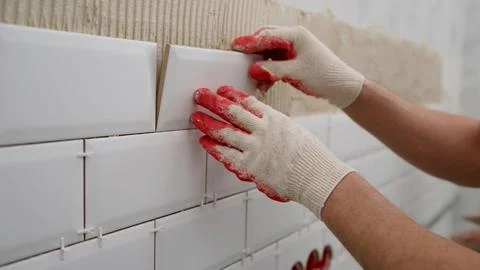 Tiler hands in the process of laying white rectangular tiles on bathroom wa.. Stock Photos