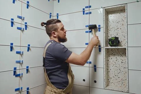 Tiler knocks the wedges of the ceramic tile leveling system off the wall in the Stock Photos