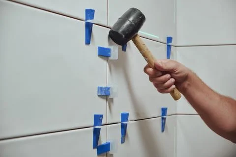 Tiler knocks the wedges of the ceramic tile leveling system off the wall in the Foto stock