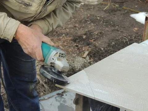 A tiler uses a grinder to remove a layer on the back side of a facing tile Stock Photos