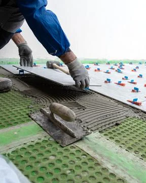 Tiler at work installing new floor with tiles. Construction. Stock Photos