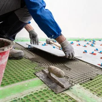 Tiler at work installing new floor with tiles. Construction. Stock Photos