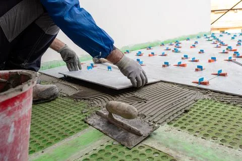 Tiler at work installing new floor with tiles. Construction. Stock Photos