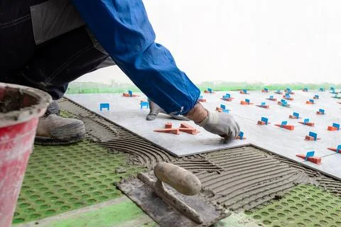 Tiler at work installing new floor with tiles. Construction. Stock Photos