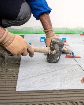 Tiler at work with rubber tile hammer. Construction. Stock Photos