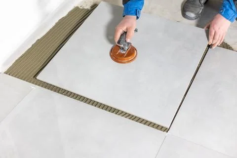 Tiler worker placing or tiling gray ceramic tile in the position over adhesive 库存照片