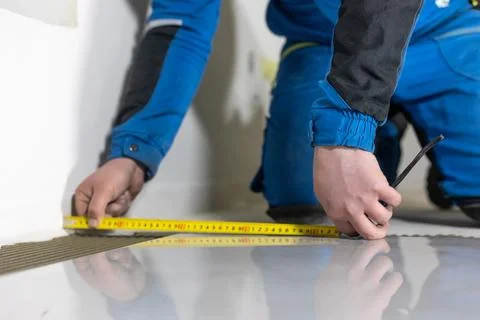 Tiler worker placing or tiling gray ceramic tile in the position over adhesive 库存照片