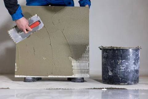 Tiler worker placing or tiling gray ceramic tile in the position over adhesive Фото