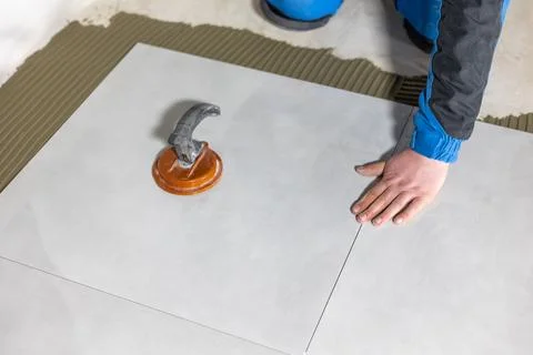 Tiler worker placing or tiling gray ceramic tile in the position over adhesive Stock Photos
