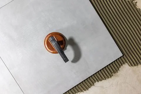 Tiler worker placing or tiling gray ceramic tile in the position over adhesive Stock Photos