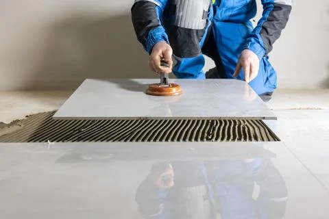 Tiler worker placing or tiling gray ceramic tile in the position over adhesive 库存照片