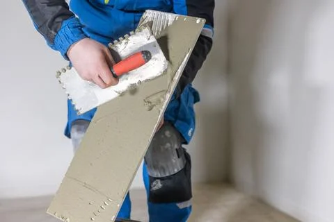 Tiler worker placing or tiling gray ceramic tile in the position over adhesive 库存照片