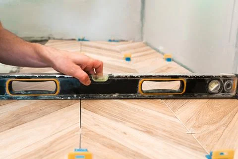 Tiling work. The man checks the level of the correct laying of the floor tiles. Stock Photos