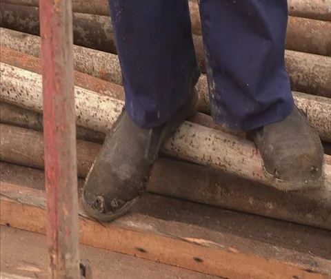 Tilt up from canvas shoes to worker in hard hat tightening bolt on scaffolding Stock Footage 86744375