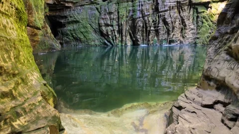 Tilt up from a clear emerald pool to a dark mysterious cave ceiling Stock Footage 340276604
