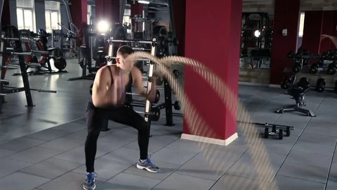 Tilt up to a closeup of a man's face working out with Battle Ropes Stockbeeldmateriaal 76526362