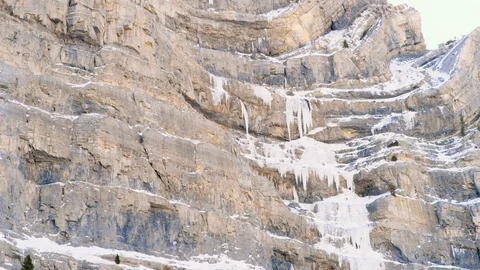Tilt down across ice covered mountainside to reveal ice climbers tiny in frame Video stock 129416209