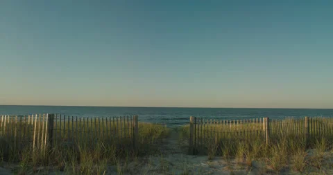 Tilt down Blue sky to New England green grassy sandy beach with fence Vidéo 212461214