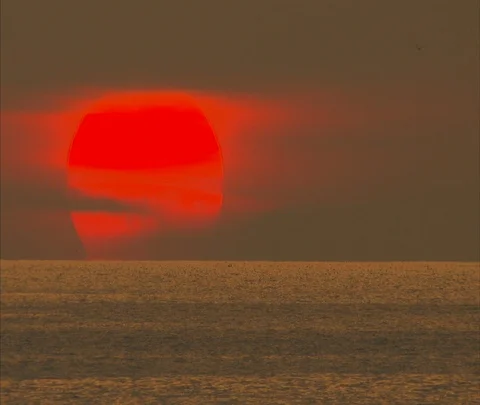 Tilt down from clouds to ocean waves breaking on beach in orange sunlight Stock Footage 86747523