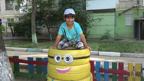 Tilt down a cute smiling child posing sitting on tires Stock Footage 117354968