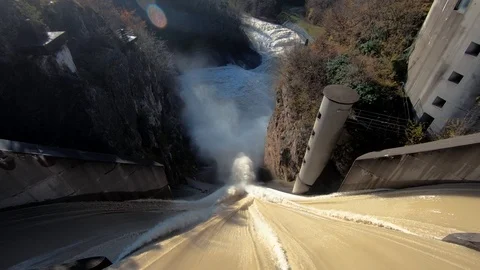 Tilt down dirty brown flooded river water flows over concrete spillway Stock Footage 120921009