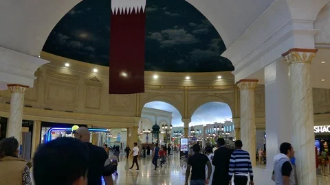 Tilt down from flag of Qatar to crowd of people walking Villaggio shopping mall Stock Footage 103948503