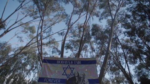 Tilt down from forest trees to posters of Israeli victims murdered at the Nova Stock Footage 297198412