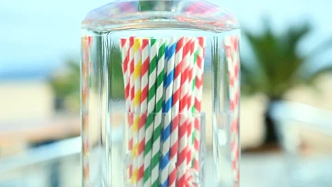 Tilt down of gin bottle biodegradable straws in a glass, beach bar background Vidéo 109420553