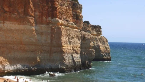 Tilt down of gold-coloured cliffs, busy beach and turquoise ocean in Benagil Stock-Footage 115939083