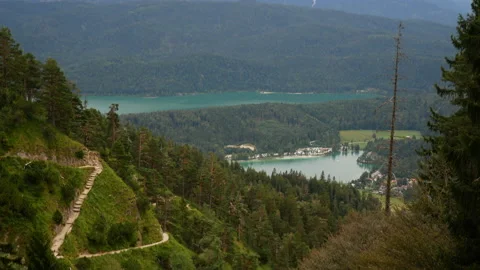 Tilt down of green mountain landscape with hiking trail and lake in background. Video stock 139606940