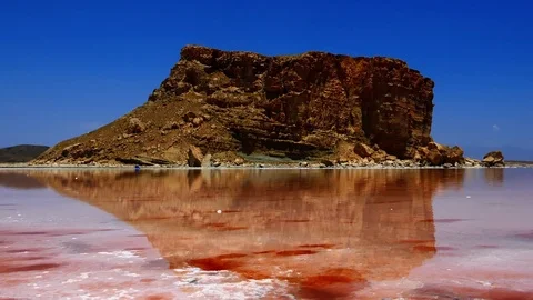 Tilt down high rock hill near red pink sea water to crystal salty beach shore Stock Footage 70355523