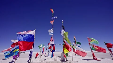 Tilt down over national flags waving above a bright salt flat Stock Footage 238628778