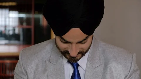 Tilt down from portrait face closeup of Sikh man with turban smiling and working Stock Footage 102420382