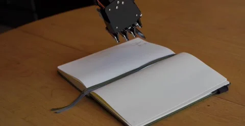 Tilt Down Of Robotic Hand After Writing AI on a Notebook Stock Footage 248090160