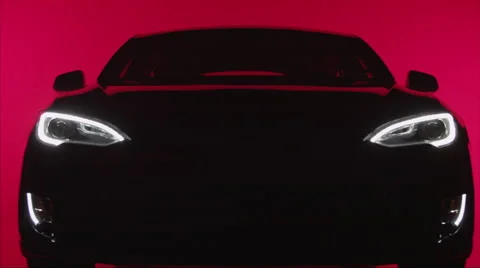 TILT down, silhouette of a sleek car against red background, headlights turn on Stock Footage