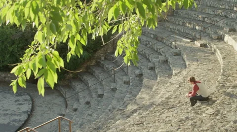 Tilt down from Tree to Man Sitting Alone in Amphitheatre Stock Footage 62653920