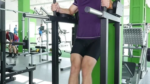 Tilt down of a young bearded man with a bare torso doing leg lifting on a Stock Footage