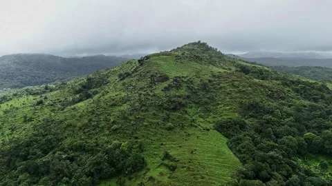 A tilt-up drone view of a large, lush green mountain under a misty, cloudy .. Video stock 314208368