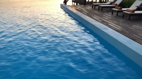 Tilt pan up to infinity pool by the ocean at sunset with palm trees Stock Footage 107575914